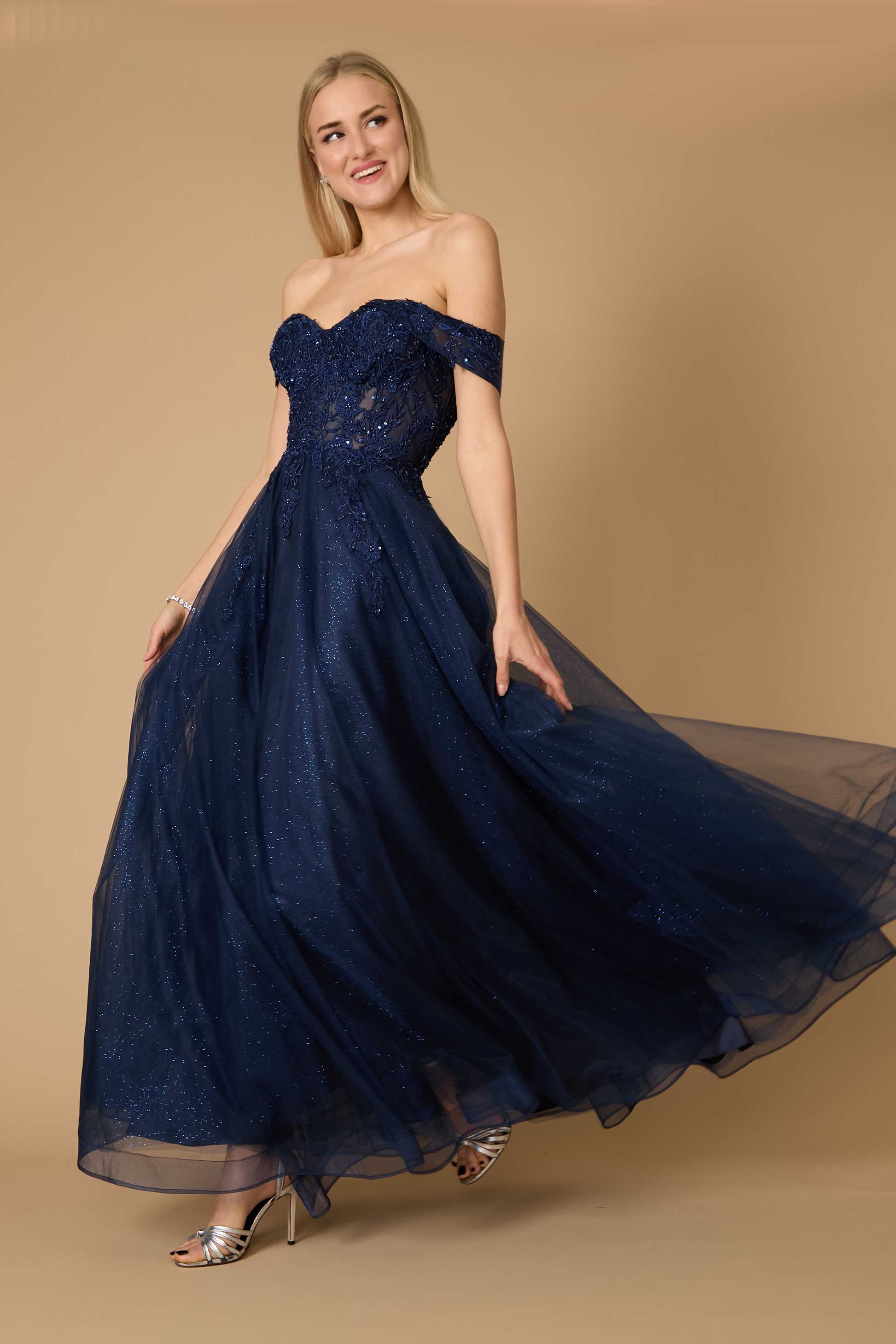 Una modelo luciendo un vestido formal largo de corsé con hombros descubiertos en color azul marino, que muestra un drapeado elegante y detalles intrincados, sobre un fondo suave y neutro.